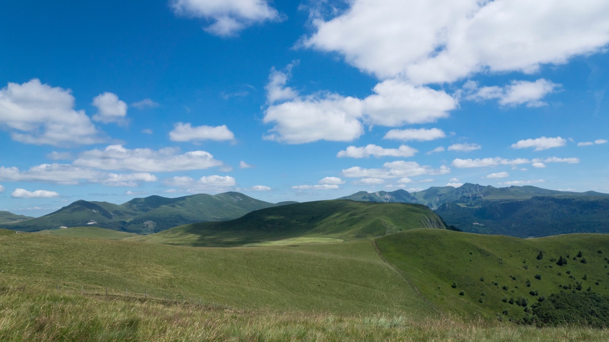 Plateau verdoyant du Cantal sous un ciel bleu