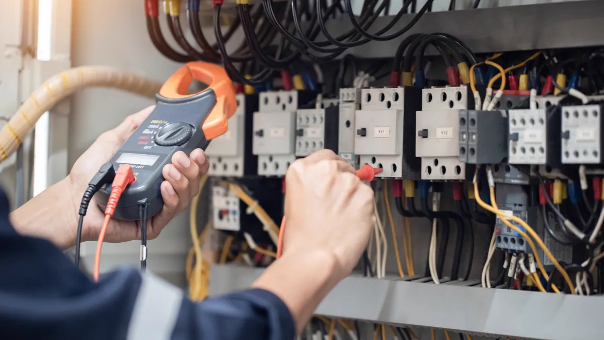 Électricien contrôlant un tableau de contacteurs à la pince ampèremétrique