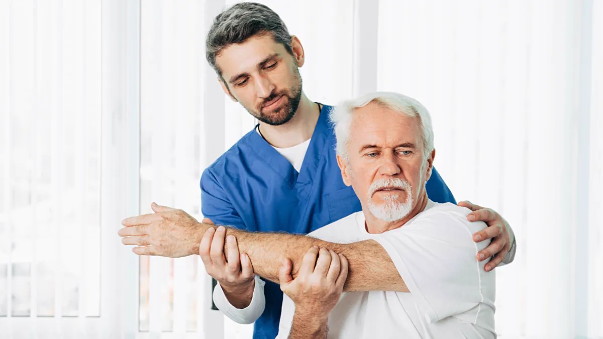 Kinésithérapeute mobilisant le bras d’un patient âgé